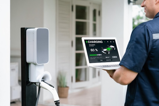 Técnico calificado que trabaja en la instalación de una estación de carga de vehículos eléctricos en el hogar, solucionando problemas y configurando el sistema de carga con una computadora portátil para vehículos eléctricos en casa Synchronos