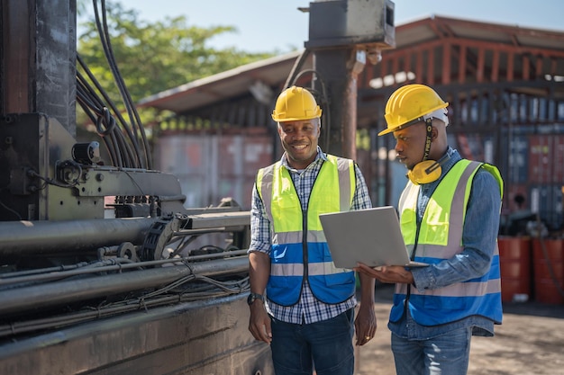 Técnico de Engenheiro Africano segurando laptop para verificar e inspecionar o motor da máquina pesada