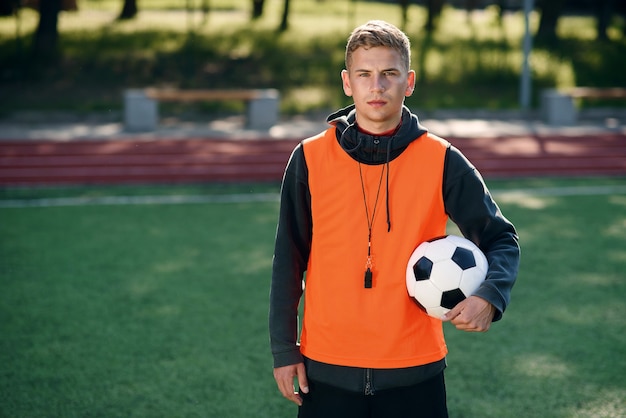 Técnico de futebol profissional com colete laranja e apito no pescoço.