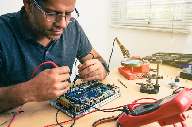 Técnico de informática usando óculos, consertando o laptop na mesa, com ferramentas ao redor. Homem negro. Ferramentas de trabalho.