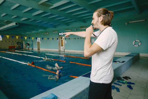 Técnico de natação masculino em pé à beira da piscina. Ele está mostrando uma mão firme para corrigir o aluno. Técnica de natação profissional.