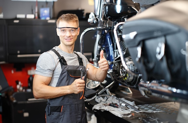 Foto técnico de reparação de motocicletas mantém os polegares para cima enquanto está na oficina