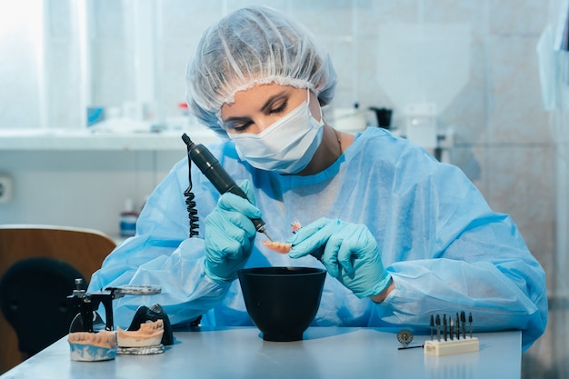 Un técnico dental enmascarado y enguantado trabaja en una prótesis dental en su laboratorio.