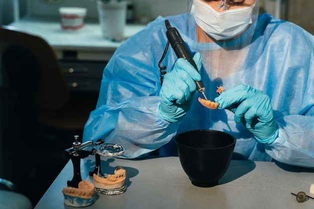 Un técnico dental enmascarado y enguantado trabaja en una prótesis dental en su laboratorio