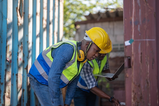 Técnico engenheiro de trabalhadores africanos segurando laptop para verificação e inspeção de contêineres no local