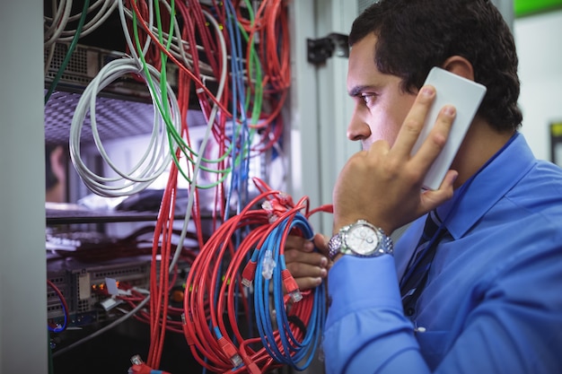 Técnico hablando por teléfono móvil mientras revisa los cables