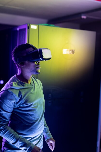 Técnico informático afroamericano con auriculares vr y trabajando en la sala de servidores