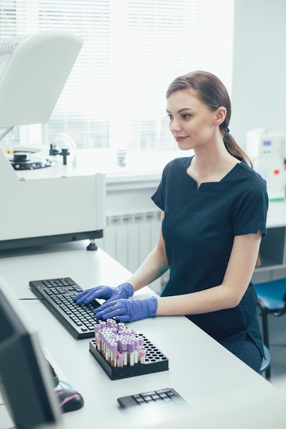 Técnico de laboratorio sonriente con guantes de goma mientras escribe en un teclado en el trabajo