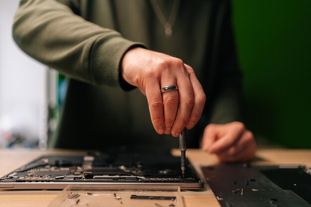 Técnico masculino reparando la placa base de la computadora portátil destornillador de precisión manipulando cuidadosamente la electrónica