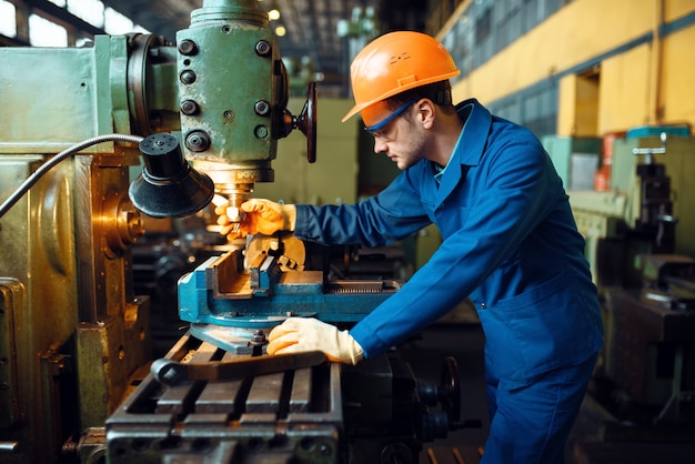 Técnico masculino en uniforme y casco trabaja en torno, planta. producción industrial, ingeniería metalúrgica, fabricación de máquinas eléctricas