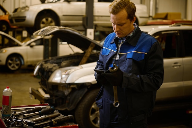 Técnico, mecánico con uniforme profesional con llave en taller de reparación. Concepto de reparación y mantenimiento de garantía de automóviles