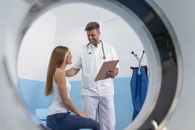 Técnico médico em pé e conversando com seu paciente sentado na cama do tomógrafo