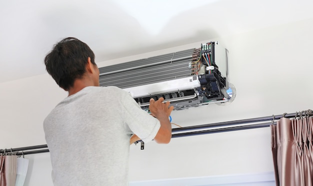 Técnico preparándose para instalar aire acondicionado nuevo en la pared blanca de la habitación