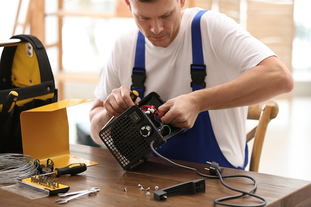 Técnico profesional que repara el calentador de ventilador eléctrico con destornillador en la mesa en el interior