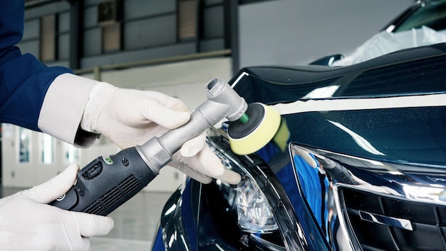 Un técnico pule la superficie de la pintura del coche con una mini máquina pulidora