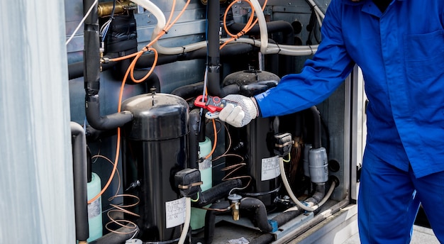 El técnico que controla las líneas eléctricas del intercambiador de calor con pinzas amperimétricas