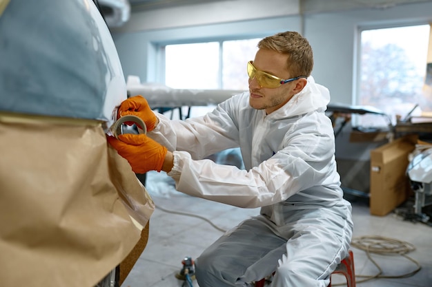 Técnico que envuelve el coche con papel artesanal protector antes de pintar. Servicio profesional de automóviles