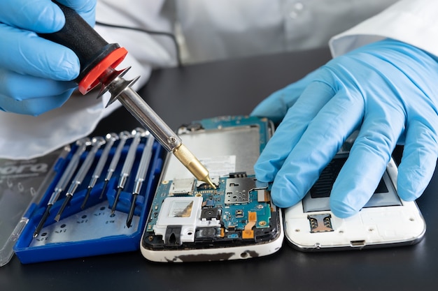 Técnico reparando el interior del teléfono móvil con soldador.