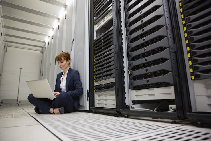Foto técnico sentado no chão ao lado da torre do servidor usando o laptop