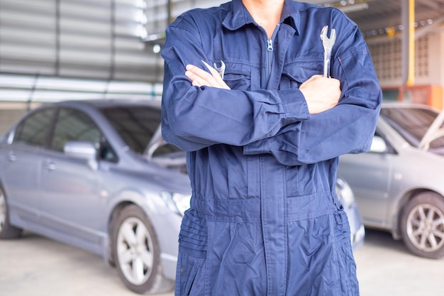 Técnico de servicio de automóviles en uniforme de pie en el fondo de un coche con un destornillador y reparación