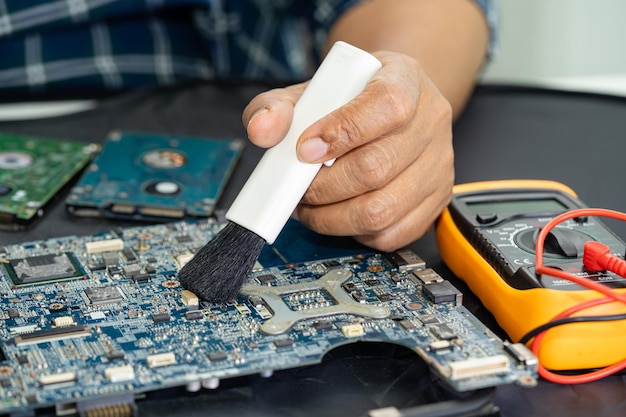El técnico usa un cepillo y una bola de aire para limpiar el polvo en la computadora de la placa de circuito Reparación de actualización y tecnología de mantenimiento