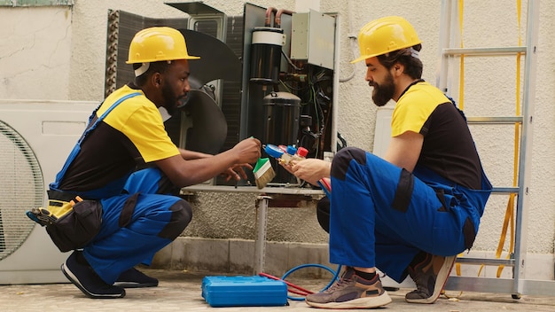 Técnicos eficientes que ensamblan medidores de colector de presión profesionales para comprobar líquidos y gases en el sistema HVAC mientras un mecánico experimentado limpia la capa de suciedad y polvo acumulados en el aire acondicionado