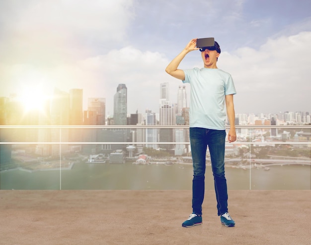 tecnologia 3d, realidade virtual, entretenimento, ciberespaço e conceito de pessoas - homem espantado com fone de ouvido de realidade virtual ou óculos 3d olhando para algo sobre fundo de arranha-céus da cidade de cingapura