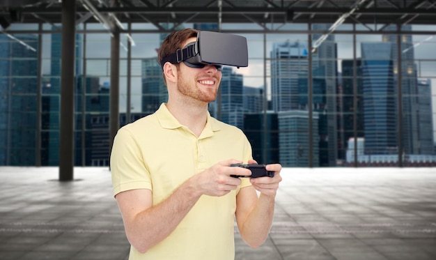 tecnologia 3d, realidade virtual, entretenimento e conceito de pessoas - jovem feliz com fone de ouvido de realidade virtual ou óculos 3d jogando com gamepad de controlador de jogo sobre sala industrial vazia