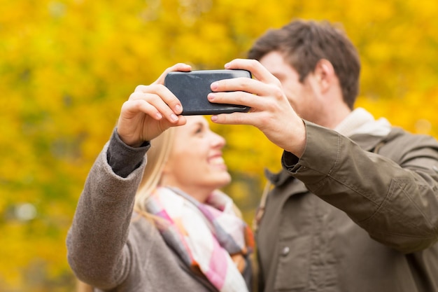 tecnología, amor, relación y concepto de personas - cerca de una pareja sonriente tomando selfie con un smartphone en el parque de otoño