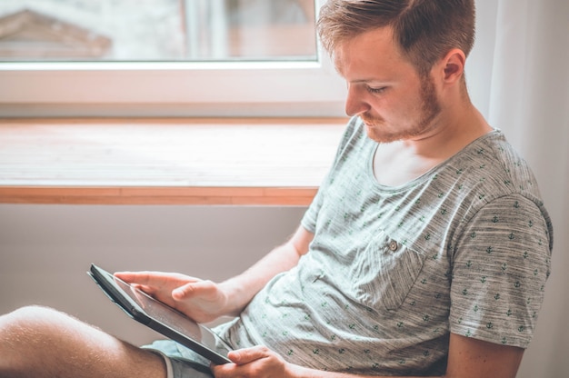 Tecnologia, casa - conceito de estilo de vida perto de um homem trabalhando com o computador tablet e sentado na cadeira em casa