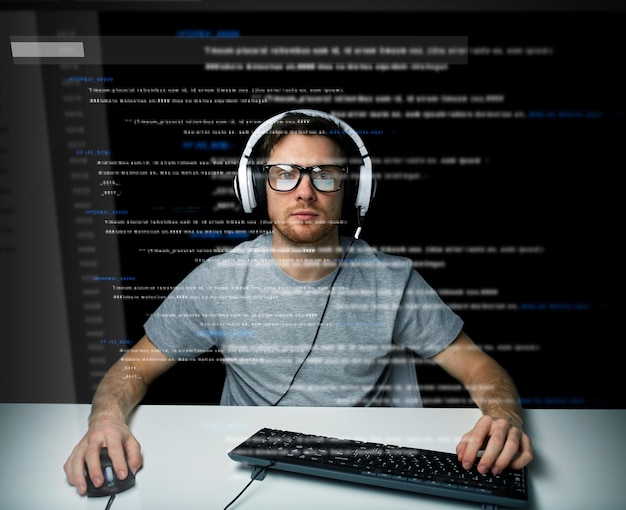 Foto tecnología, ciberespacio, realidad virtual y concepto de personas - hombre o hacker en auriculares y anteojos con sistema informático de piratería de teclado o programación sobre proyección de pantalla virtual