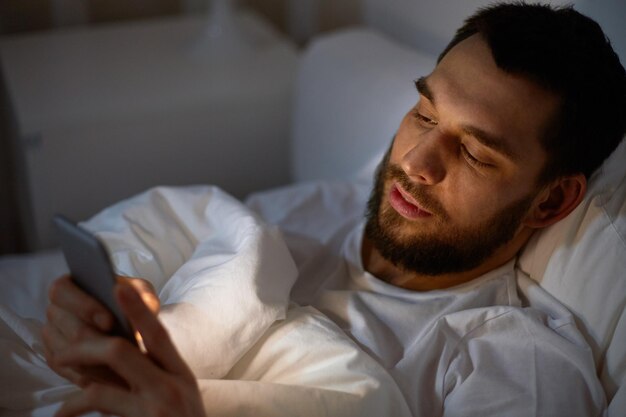 tecnologia, comunicação e conceito de pessoas - homem enviando mensagens de texto no smartphone na cama em casa à noite