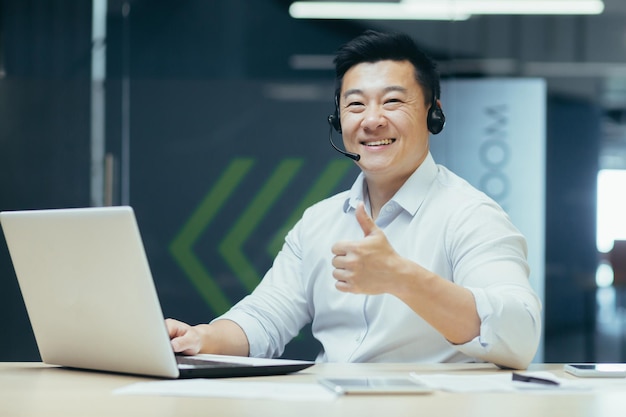 Tecnologia de suporte trabalhadora de empresário asiático bem-sucedido com fone de ouvido para videochamada olhando para a câmera