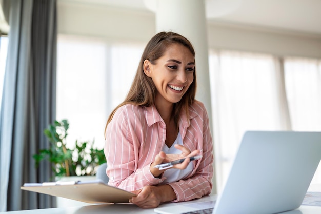 Tecnologia de trabalho remoto e conceito de pessoas feliz sorridente jovem mulher de negócios com computador portátil e papéis trabalhando em escritório em casa