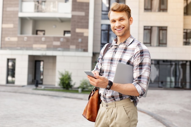 Tecnología digital. Joven inteligente sosteniendo su computadora portátil mientras usa un teléfono inteligente al mismo tiempo