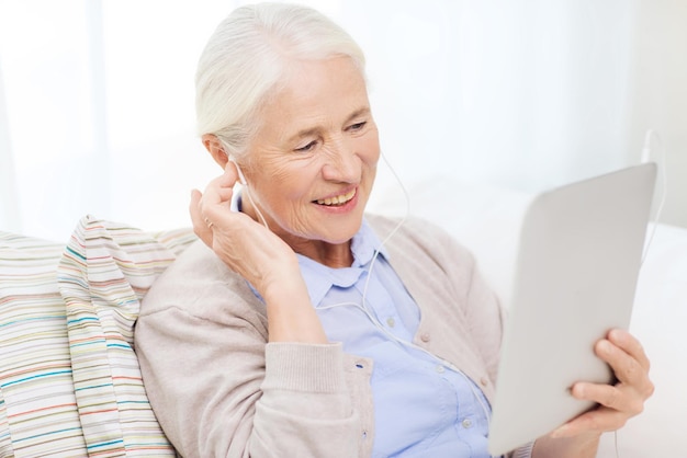 tecnología, edad y concepto de la gente - feliz anciana con tablet pc y auriculares escuchando música en casa