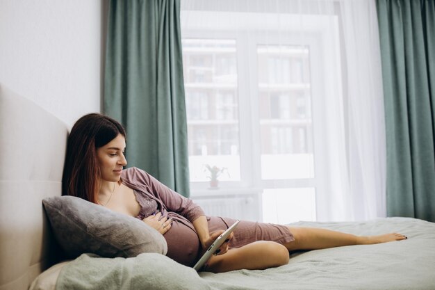 Tecnología de embarazo personas y concepto de expectativa cerca de una mujer embarazada con una computadora de tablet pc en la cama en casa