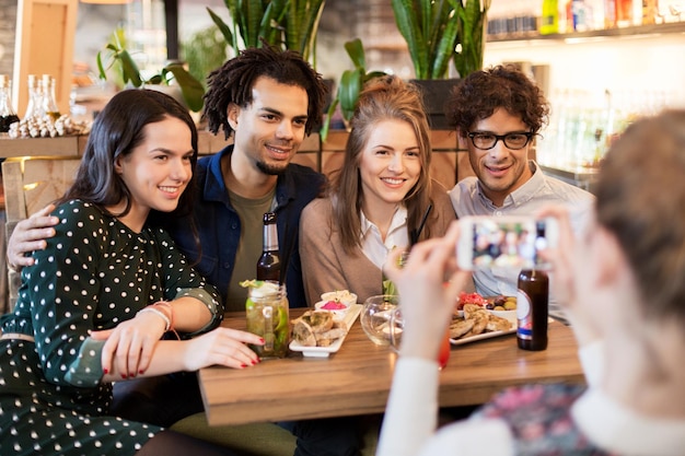 tecnologia, estilo de vida e conceito de pessoas - amigos felizes com smartphone fotografando em bar ou café