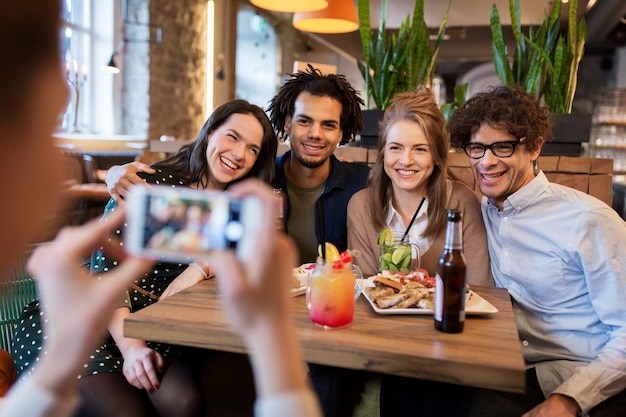 tecnologia, estilo de vida e conceito de pessoas - amigos felizes com smartphone fotografando em bar ou café