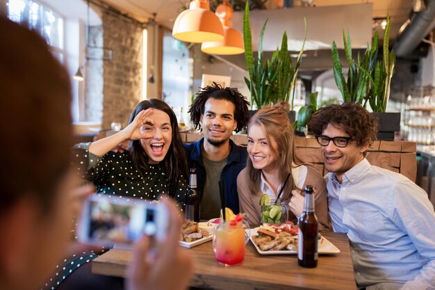 Foto tecnologia, estilo de vida e conceito de pessoas - amigos felizes com smartphone fotografando em bar ou café