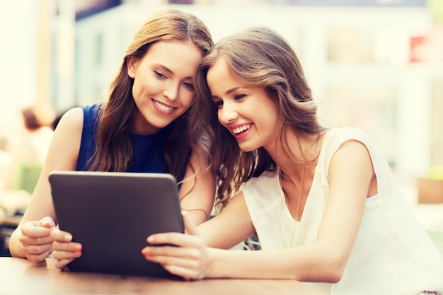 tecnología, estilo de vida, amistad y concepto de personas - mujeres jóvenes felices o adolescentes con tablet pc en un café al aire libre