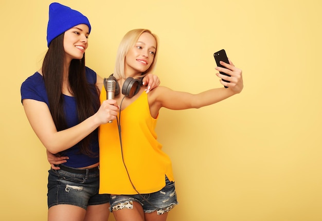 Tecnología de estilo de vida y concepto de personas Chicas felices con teléfono inteligente sobre fondo amarillo Selfie feliz