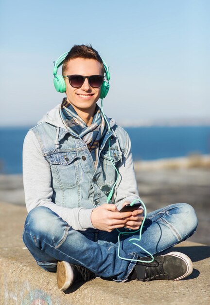 tecnología, estilo de vida y concepto de personas: joven sonriente o adolescente con auriculares con smartphone escuchando música al aire libre