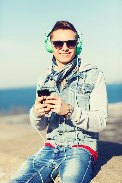 tecnología, estilo de vida y concepto de personas: joven sonriente o adolescente con auriculares con smartphone escuchando música al aire libre