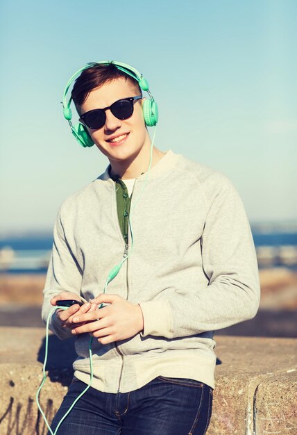 tecnología, estilo de vida y concepto de personas: joven sonriente o adolescente con auriculares con smartphone escuchando música al aire libre