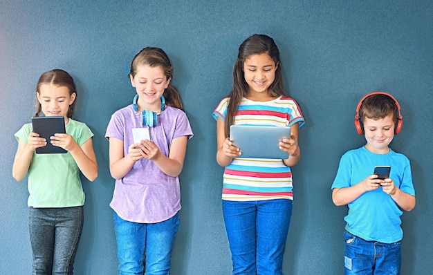 Tecnología de estudio y grupo de niños para educación electrónica e investigación en línea con sonrisa Estudiantes felices niñas y niños con aplicación digital de tabletas, teléfonos inteligentes y auriculares con fondo azul