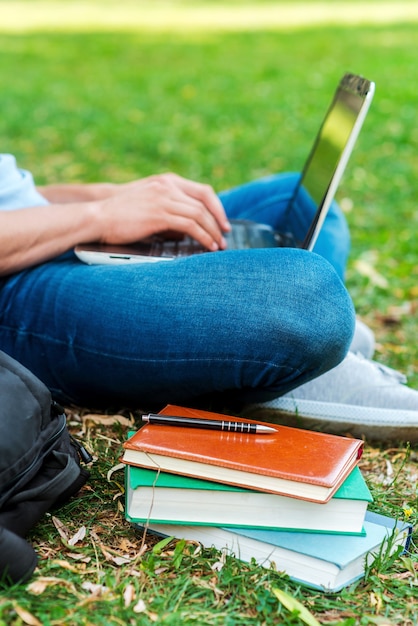 La tecnología facilita el estudio. Primer plano de un estudiante que trabaja en la computadora portátil mientras está sentado en el césped