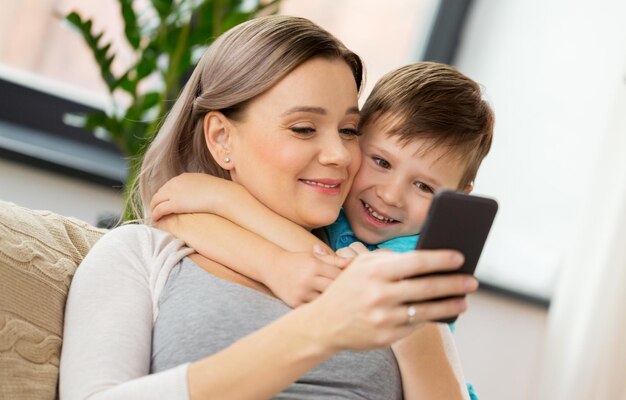 tecnología familiar y concepto de personas madre feliz y hijo pequeño con teléfono inteligente en casa