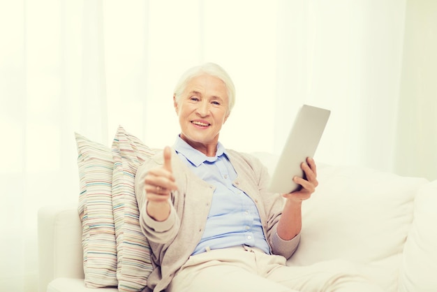 tecnologia, idade, gesto e conceito de pessoas - mulher sênior feliz com computador tablet pc mostrando os polegares em casa