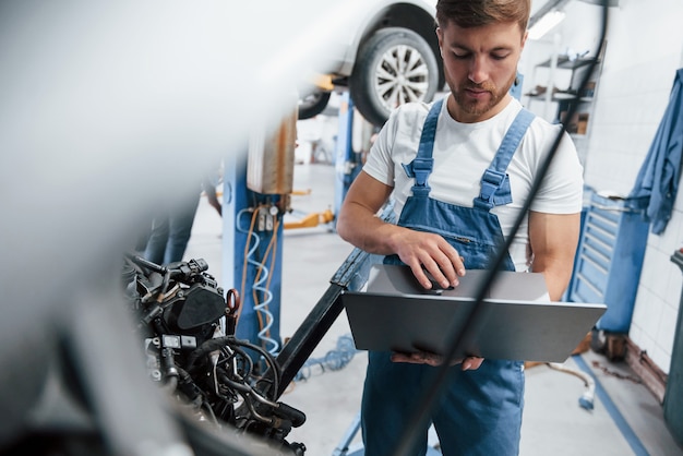 Tecnología inalámbrica. Empleado con uniforme de color azul trabaja en el salón del automóvil.